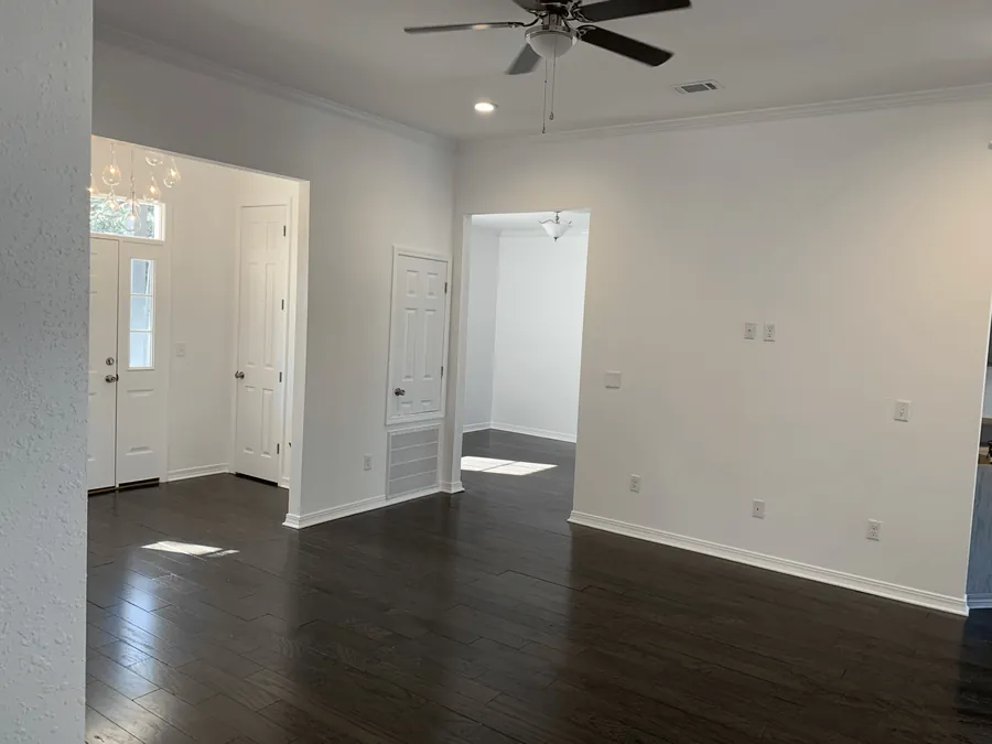 Bright open living area with dark wood floors, a ceiling fan and an arched entry to the foyer