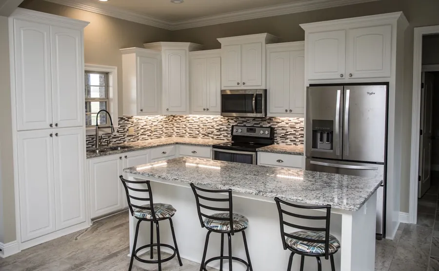 White kitchen with a granite island, bar stools, mosaic backsplash and stainless appliances